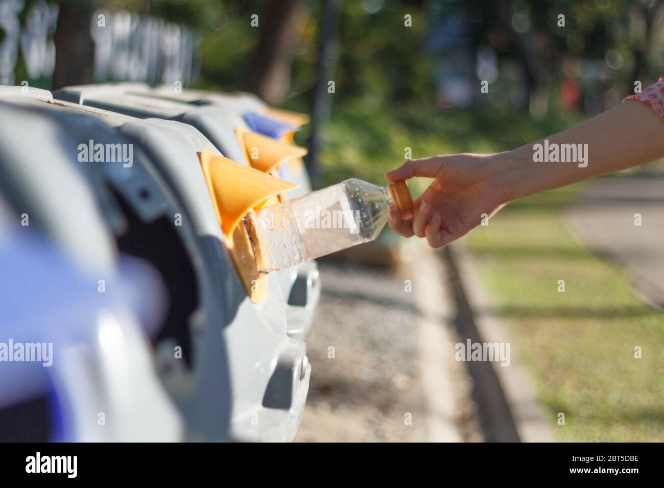 Closeup donna mano gettando bottiglia vuota di plastica in contenitore di riciclaggio. Isolato esterno sfondo. Foto Stock