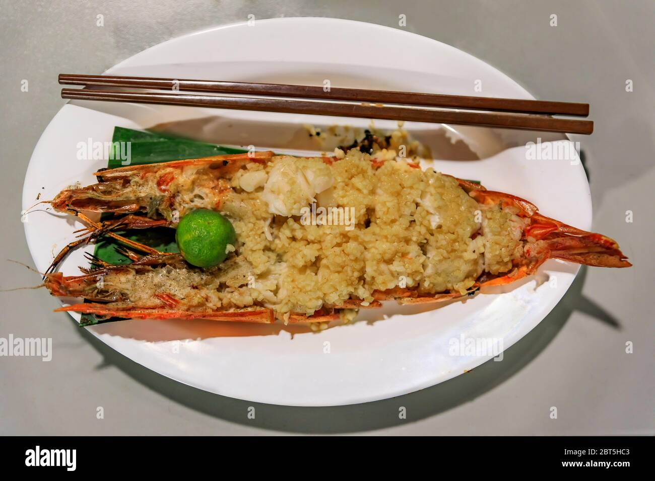 Gamberi grandi o gamberetti freschi grigliati con aglio e lime arrostiti su un piatto con bastoncini di pollo presso una bancarella di Singapore Foto Stock