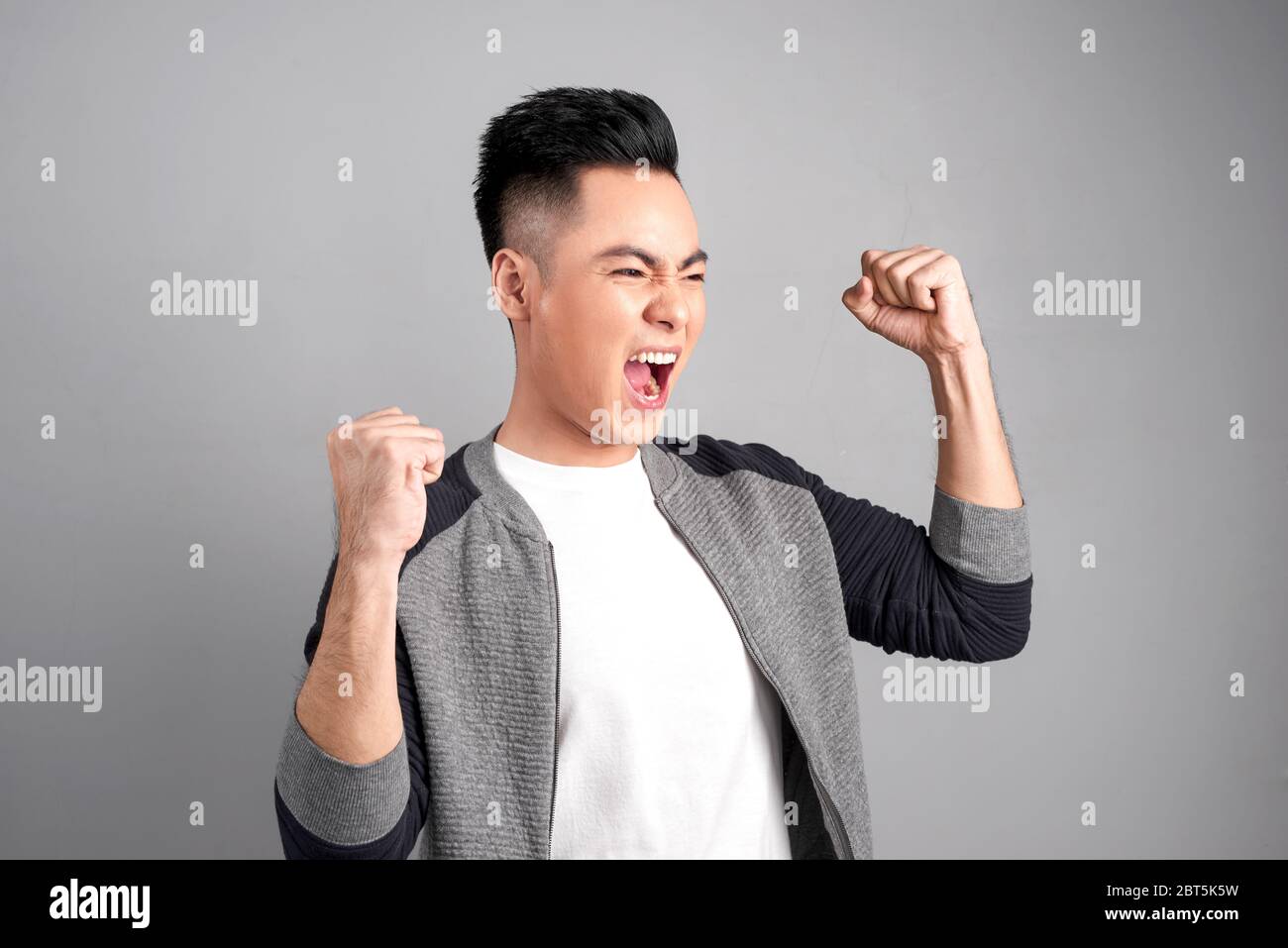 Uomo d'affari di successo gridando con le braccia fino a suggerire il suo adempimento, isolato su sfondo grigio. Foto Stock