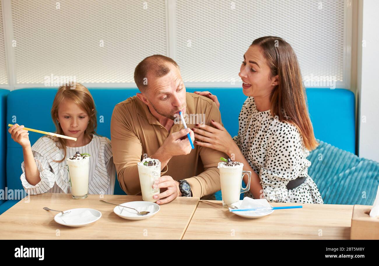 Felice famiglia padre, madre e figlia sta divertendosi nel locale caffè, seduto nel caffè sul divano blu, milkshakes sul tavolo Foto Stock