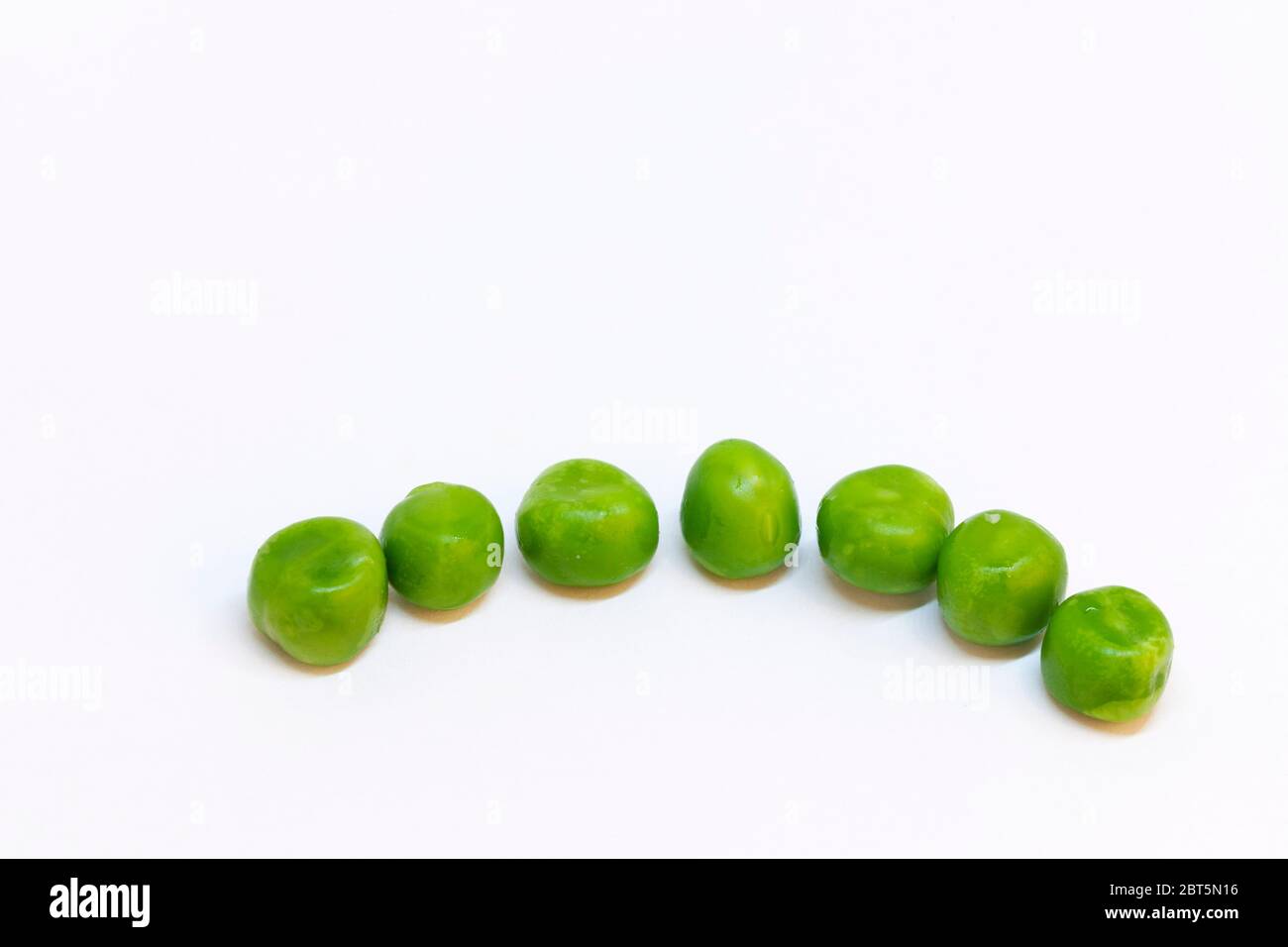piselli verdi su una fila su sfondo bianco Foto Stock