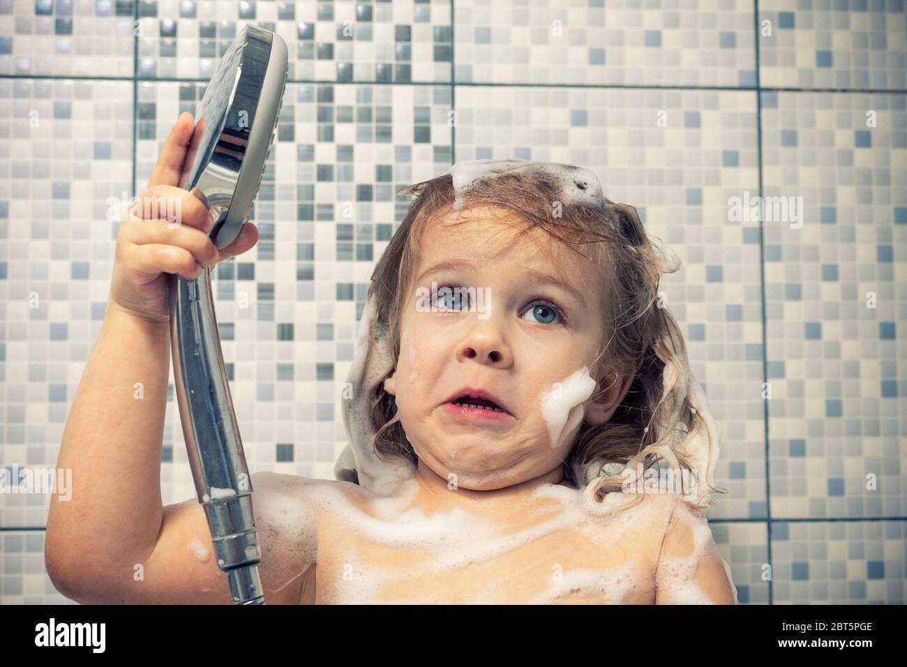 una bambina in schiuma è in piedi nella vasca da bagno in mano tenendo una  doccia, non c'è acqua. il bambino non può lavare il sapone, emozionalmente  reagisce Foto stock - Alamy