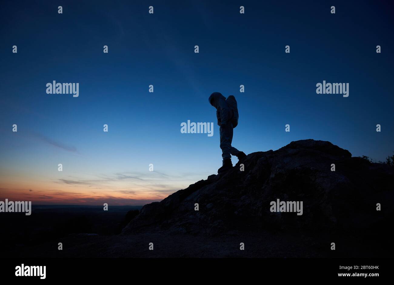 Splendida vista del viaggiatore di spazio su montagne rocciose con maestoso cielo notturno sullo sfondo. Silhouette di cosmonaut in tuta spaziale esplorando il nuovo pianeta. Concetto di viaggio spaziale e bellezza al crepuscolo. Foto Stock