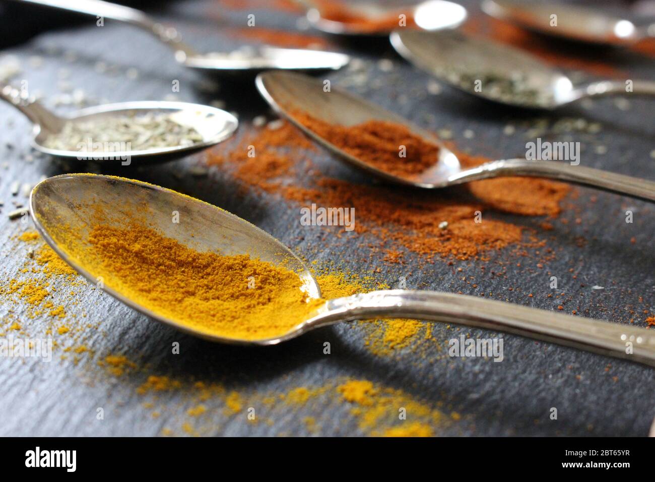 Una fotografia di cucchiaini di varie erbe, spezie e semi su uno sfondo di ardesia. Ingredienti crudi per cucinare Foto Stock