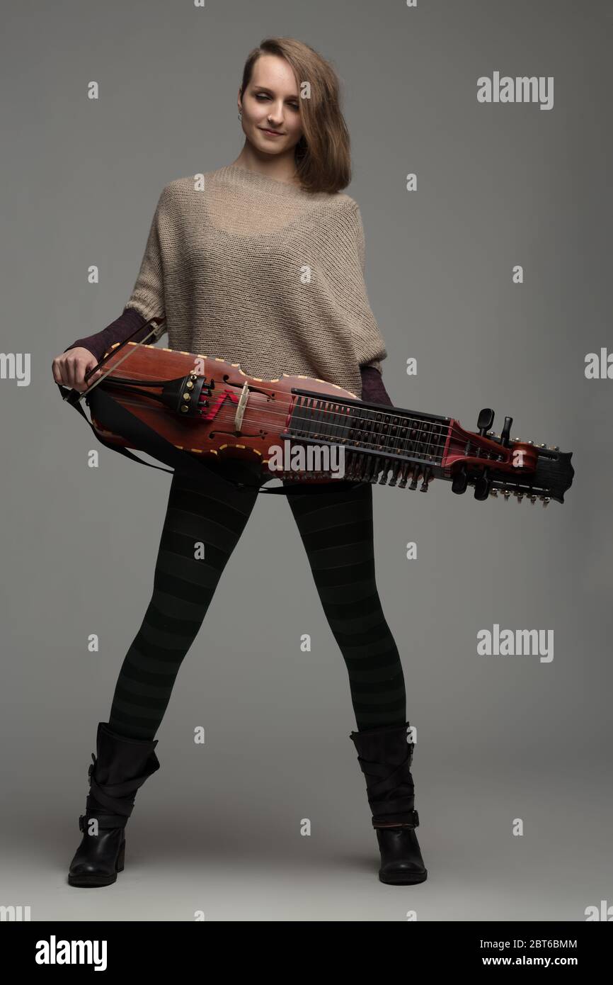 Attraente musicista moderna e di stile con una ricostruzione contemporanea di uno strumento svedese nyckelharpa con corde su uno studio grigio Foto Stock