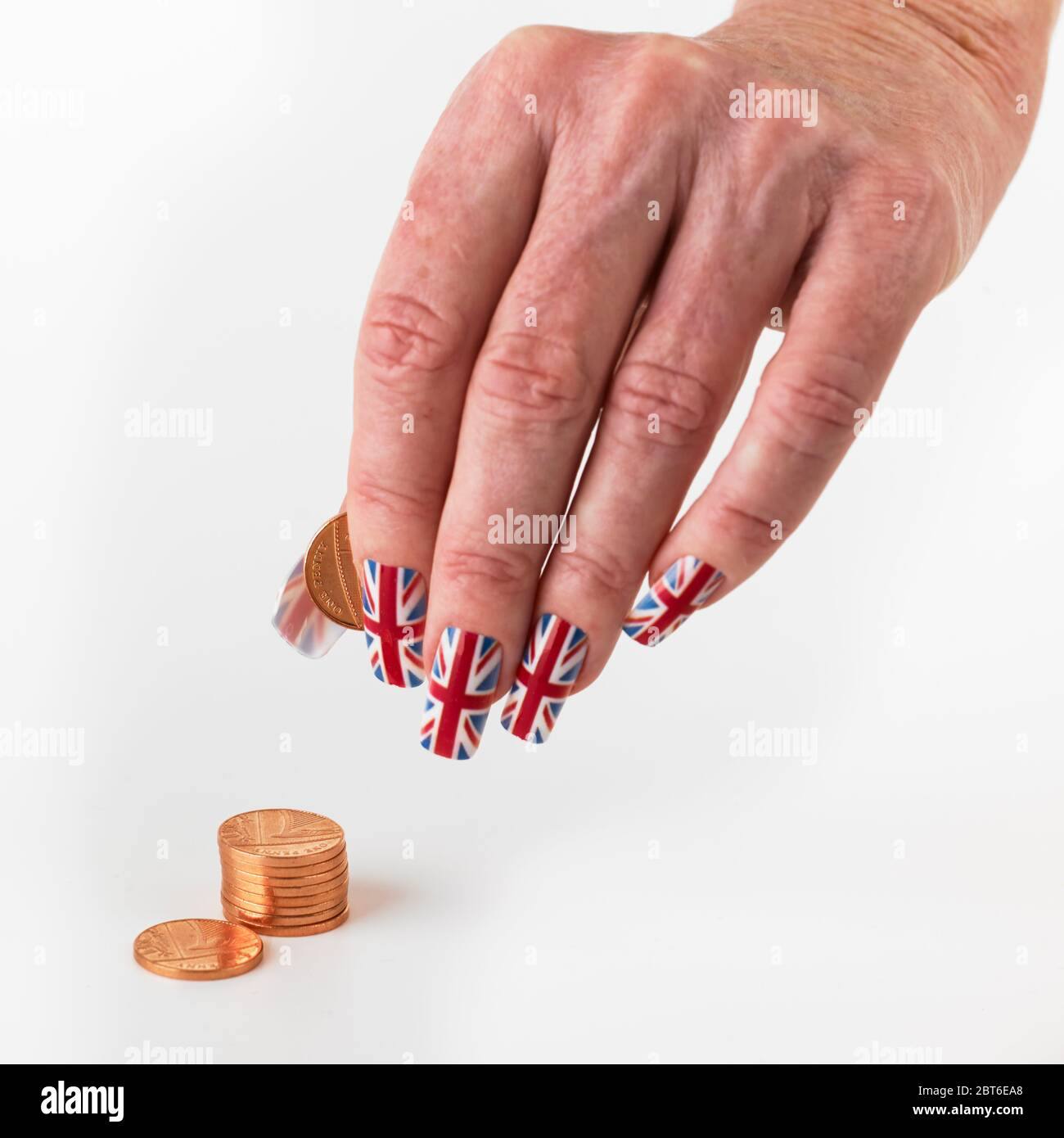 Mano che indossa bandiera Union falsi chiodi che tengono sterling moneta piccola su sfondo bianco Foto Stock