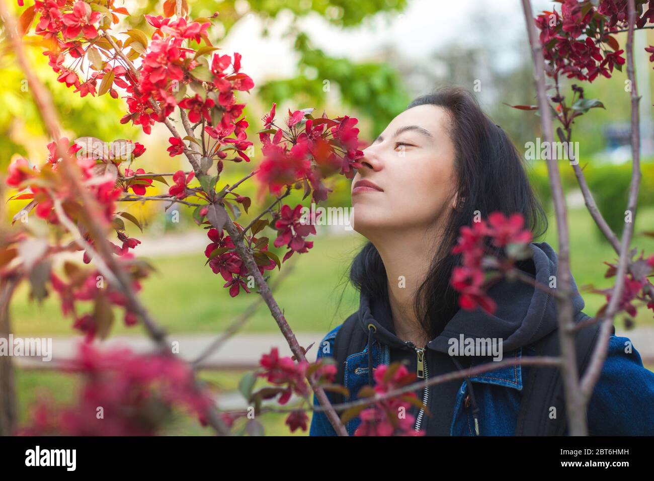 Giovane ragazza che sniffing fiori con petali rosa in una passeggiata nel parco Foto Stock
