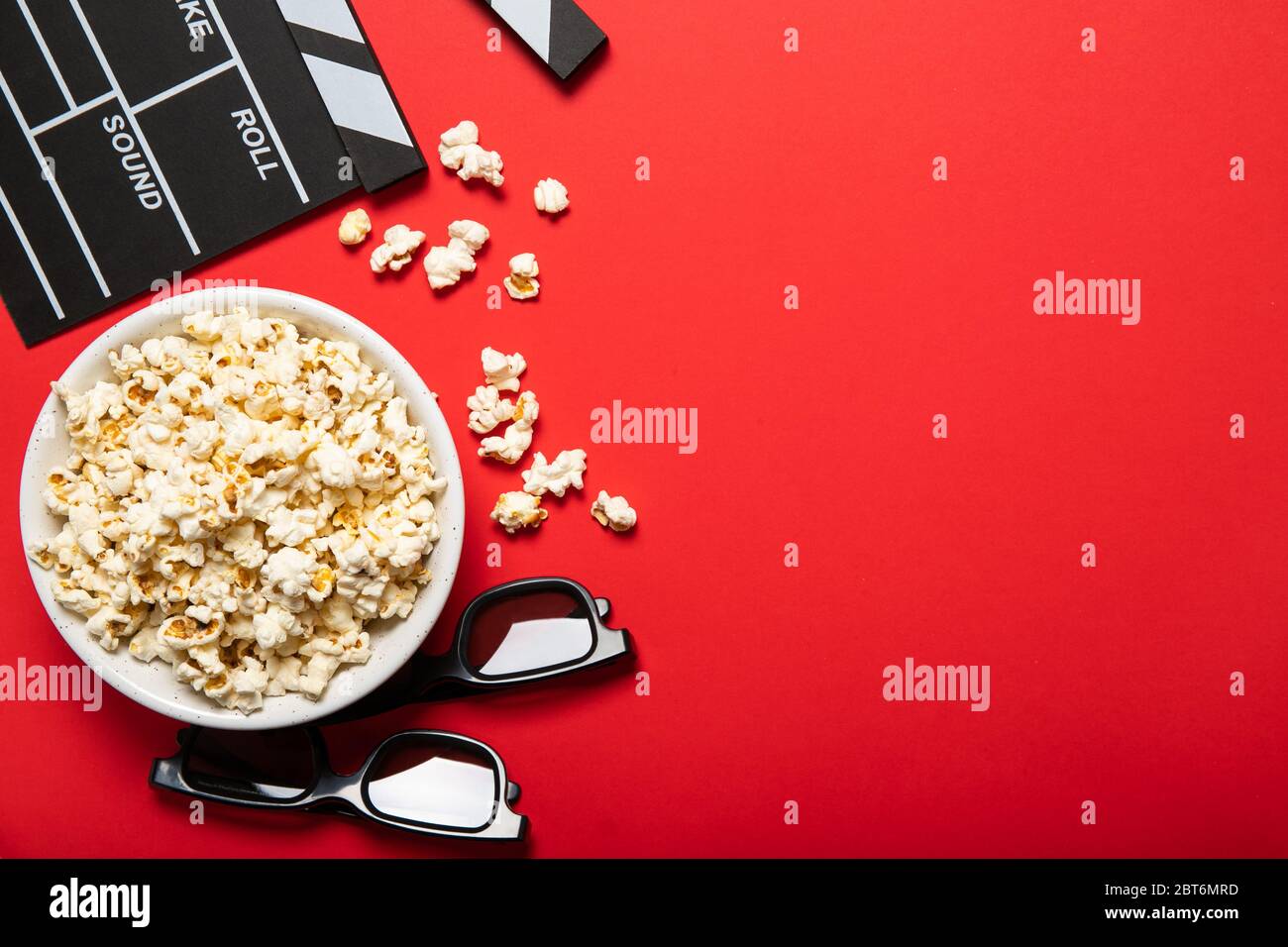 Piatto con popcorn e clapper di film su sfondo rosso. Posiziona per il testo Foto Stock