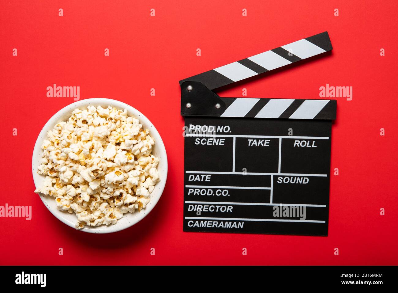 Piatto con popcorn e clapper di film su sfondo rosso Foto Stock