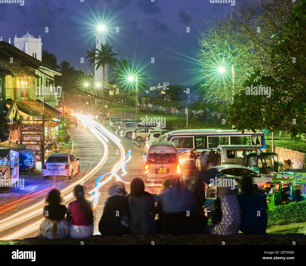 Foto notturna di strada trafficata a Fort Galle, Sri Lanka, con sentieri leggeri dalle auto di passaggio e il famoso faro di Galle all'estremità della fra Foto Stock
