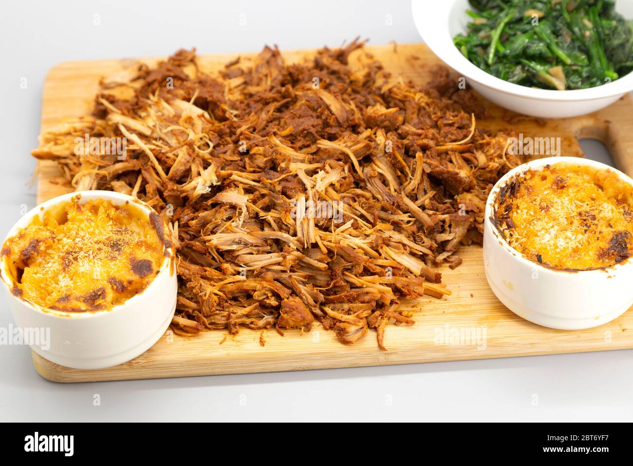 Maiale tirato homecoked servito sminuzzato su un asse di legno. Il piatto è servito con mac e formaggio e spinaci saltati. Foto Stock