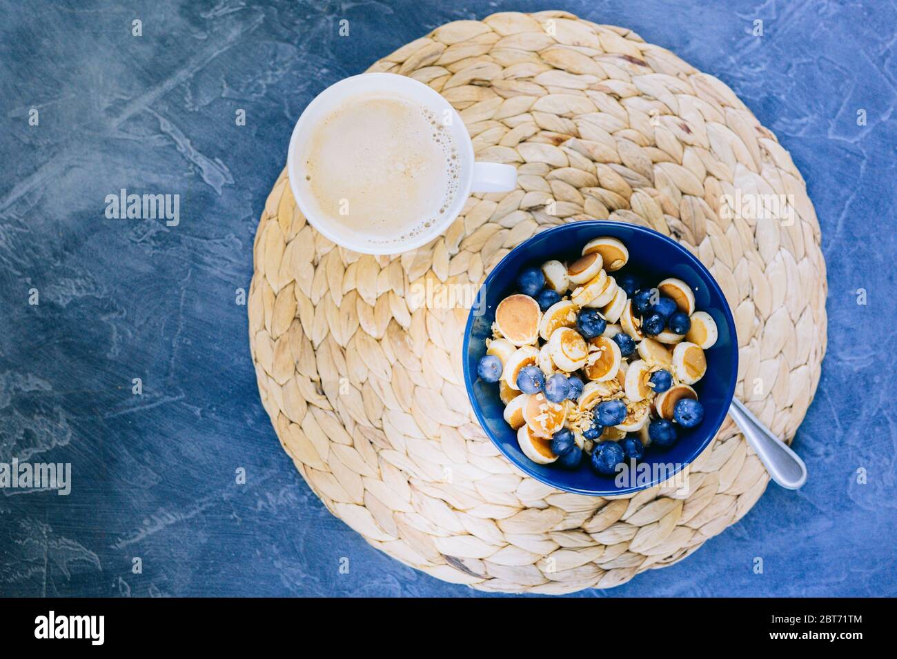Mattina, colazione, mini pancake ai cereali, mini pancake in una ciotola blu scuro con miele di sciroppo d'acero con mirtillo e tazza di caffè. Cibo Foto Stock
