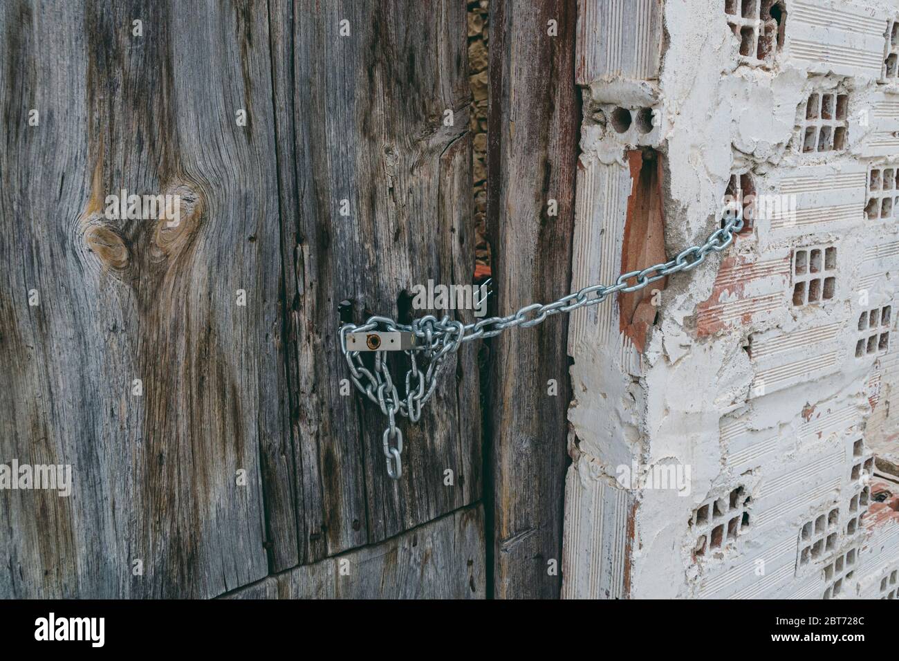 Cancello in legno arrugginito, catena e lucchetto appesi alla porta. Casa abbandonata. Vecchio cancello e lucchetto. Foto Stock