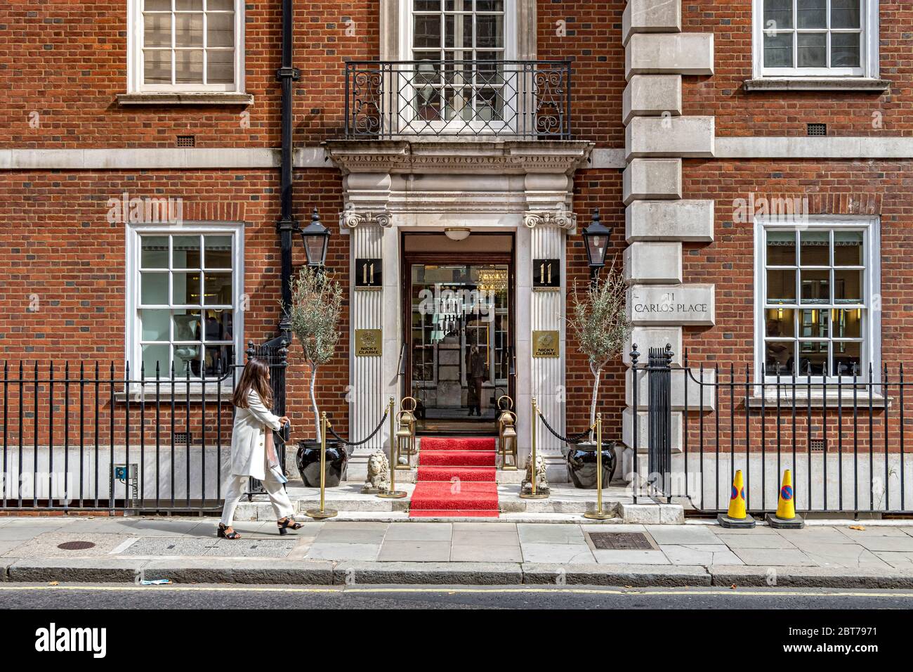Una donna cammina oltre l'entrata al parrucchiere di Nicky Clarke Mayfair su Carlos Place, Mayfair, Londra W1 Foto Stock