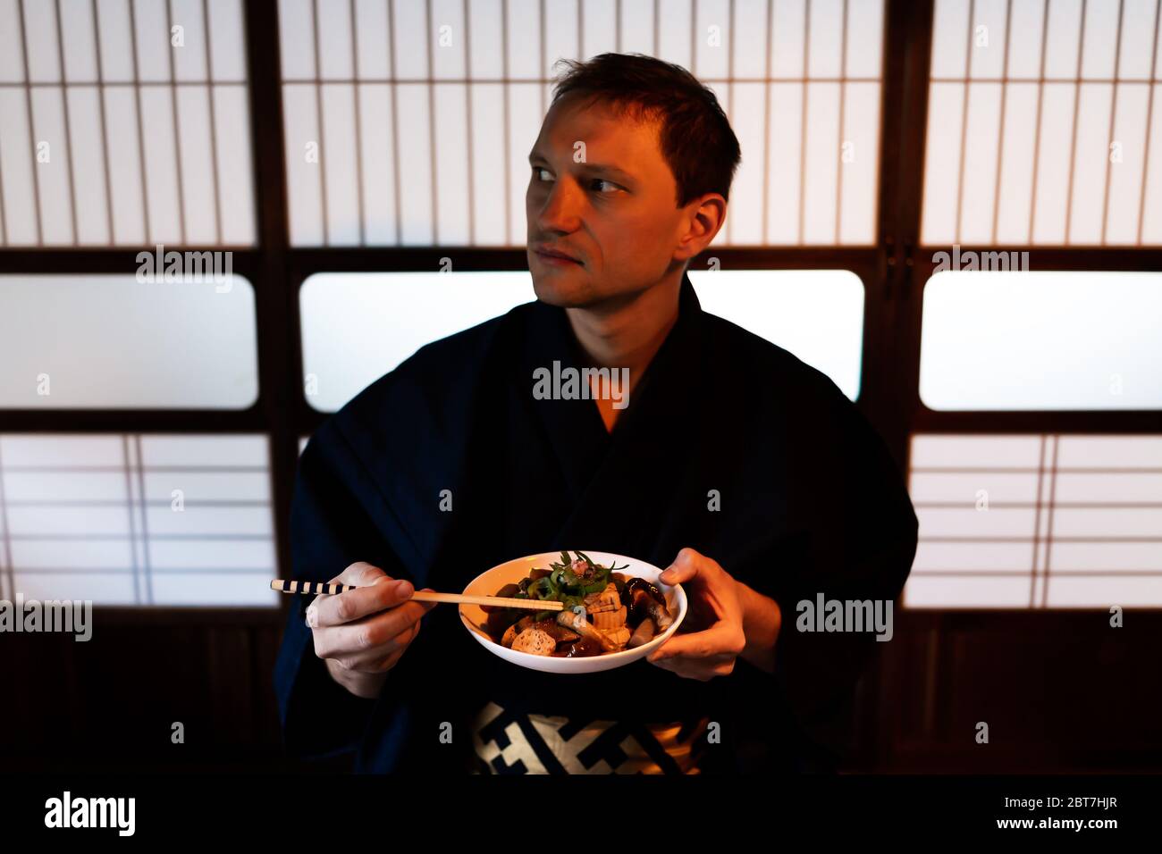Tradizionale casa ristorante giapponese ryokan con closeup di uomo in kimono o yukata mangiare piatto konnyaku con porte di carta scorrevole shoji in background Foto Stock