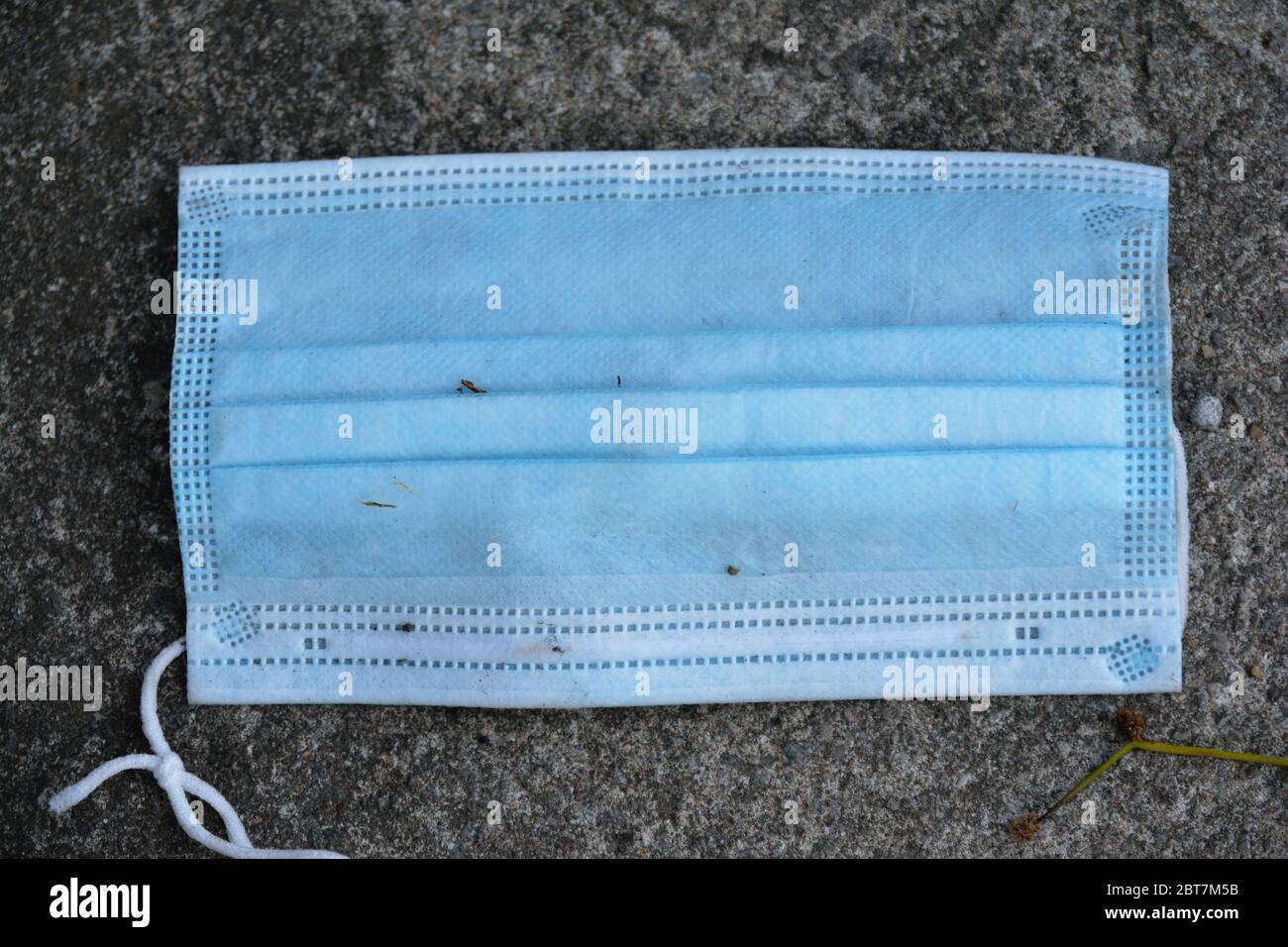 una maschera chirurgica monouso usata che si trova a terra Foto Stock