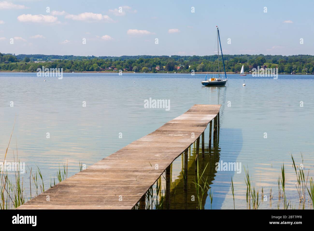 Molo in legno e barca a vela ad Ammersee (Lago Ammer). Cielo limpido con poche nuvole bianche. Simbolo per relax, ricchezza, attività di svago. Formato panorama Foto Stock