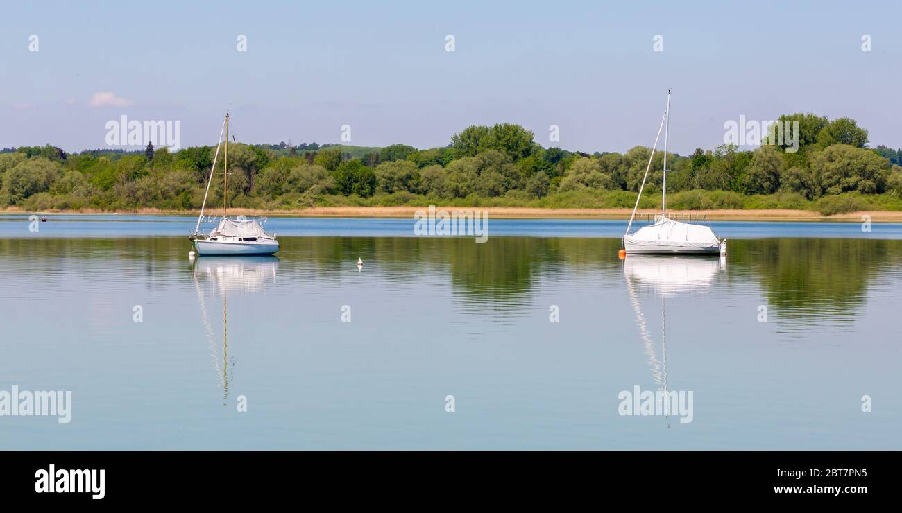 Bellissimo panorama di Ammersee con due barche a vela. Con riflessi d'acqua. Lussureggiante foresta verde sullo sfondo. Paesaggio superiore bavarese. Foto Stock