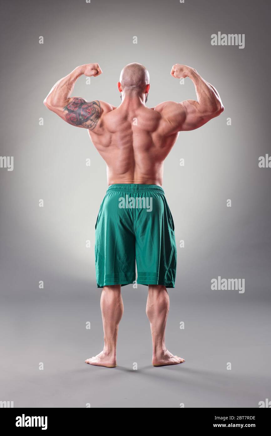 Bodybuider muscolare sexy in posa su sfondo grigio. Vista posteriore Foto Stock