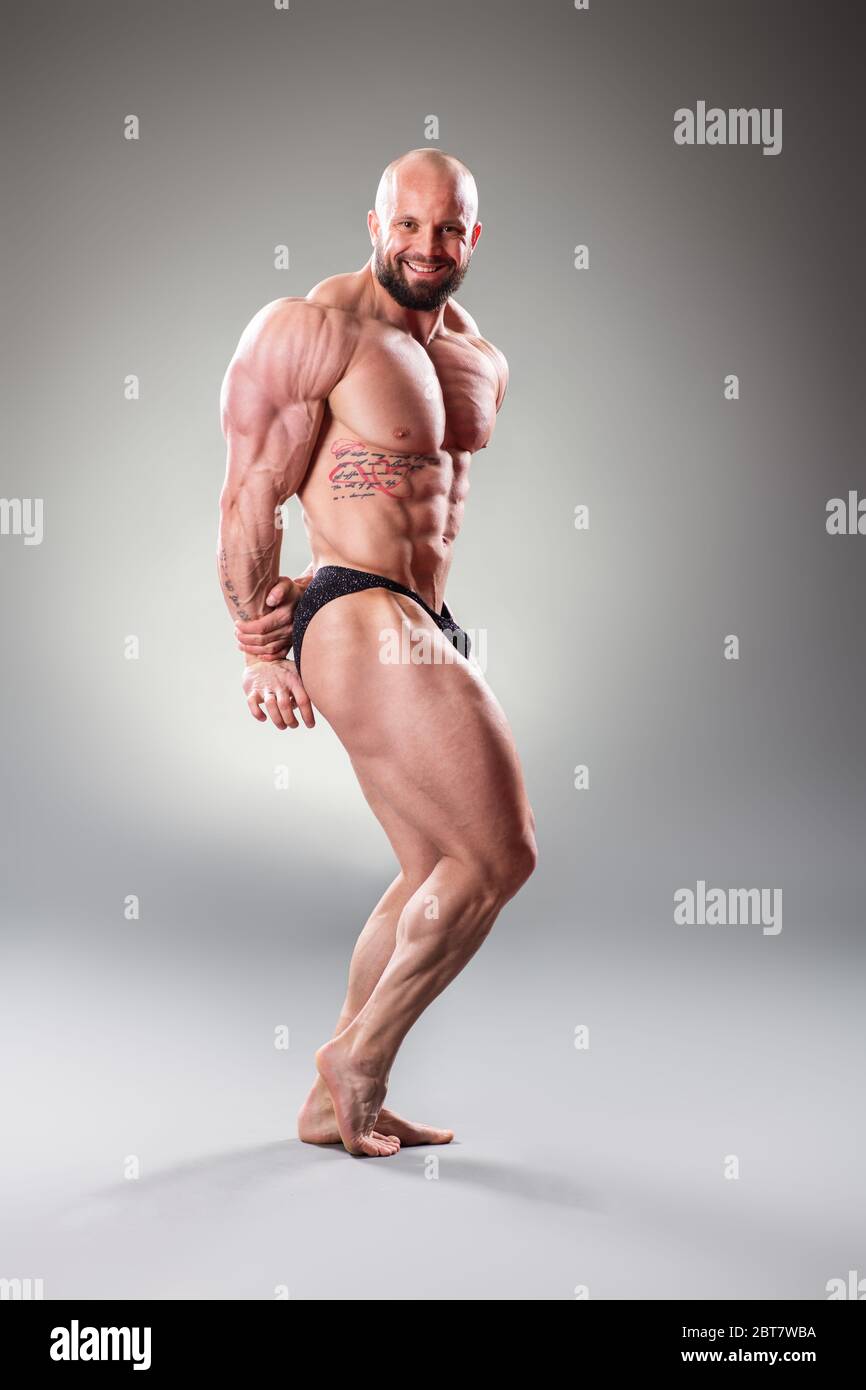 Bodybuider muscolare sexy in posa su sfondo grigio Foto Stock