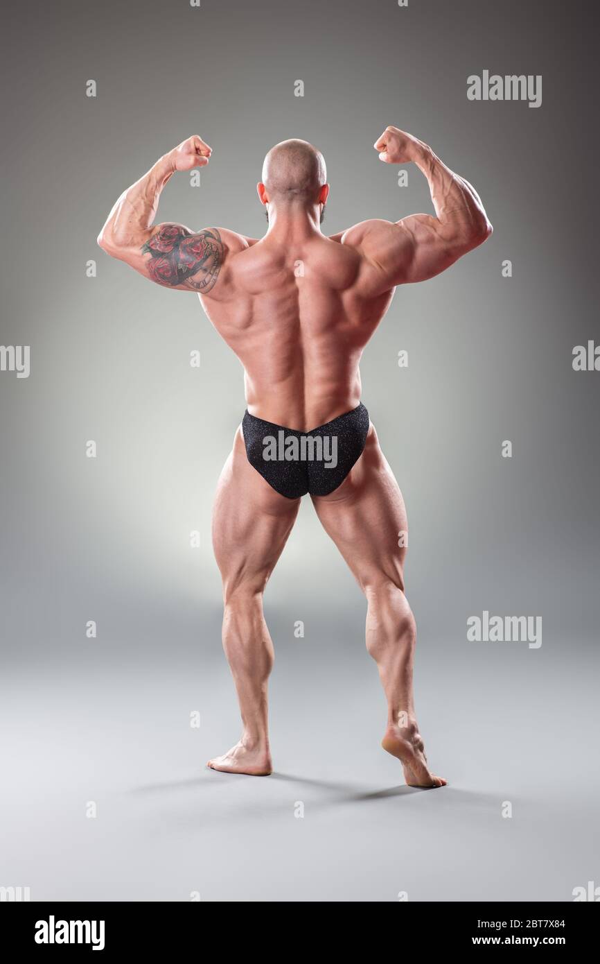 Bodybuider muscolare sexy in posa su sfondo grigio. Vista posteriore Foto Stock