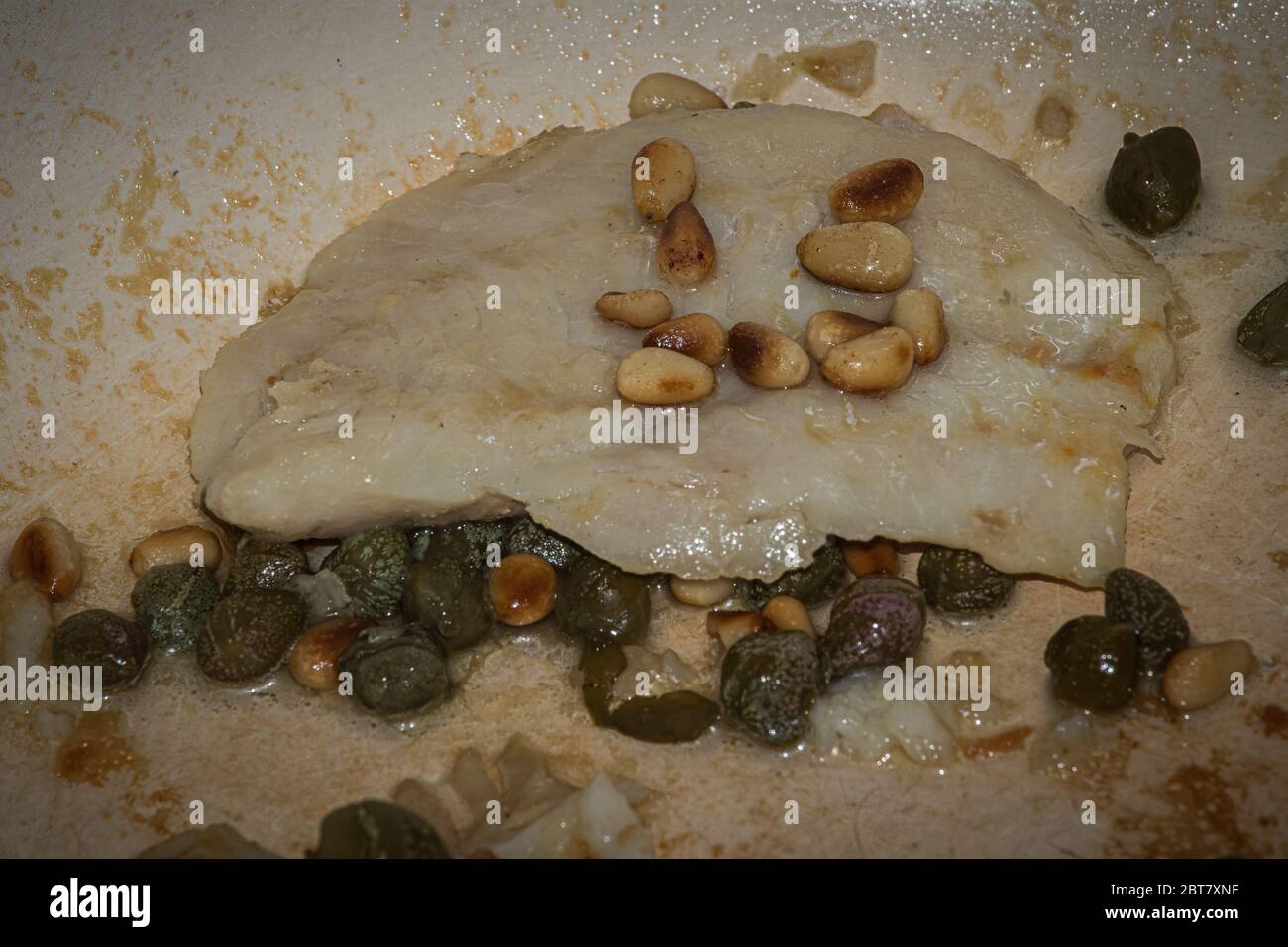 immagine ravvicinata di una fetta di pesce fritto in padella con pinoli e capperi Foto Stock