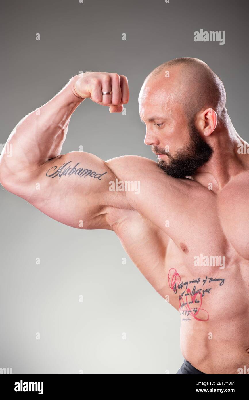 Bodybuider muscolare sexy in posa su sfondo grigio. Contrazione dei bicipiti Foto Stock