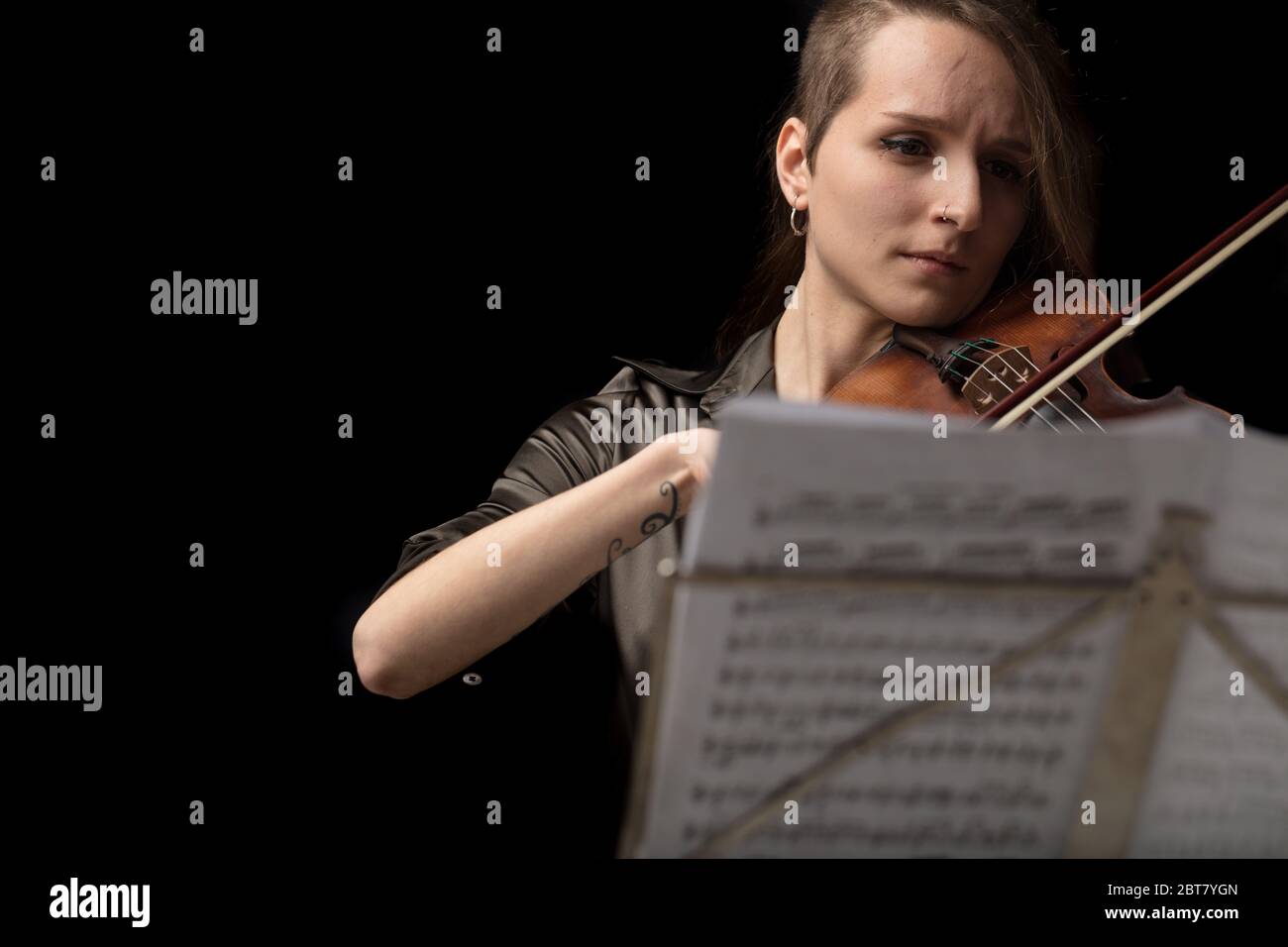 Donna violinista che suona in un recital classico su un violino barocco, visto sopra la parte superiore di una spartito musicale su uno stand di ottone durante lo spettacolo dal vivo Foto Stock