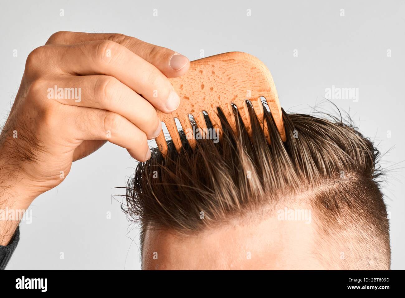 Giovane uomo che piega i capelli con un pettine di legno. Styling dei  capelli a casa. Concetto di pubblicità di shampoo per capelli sani e contro  forfora Foto stock - Alamy