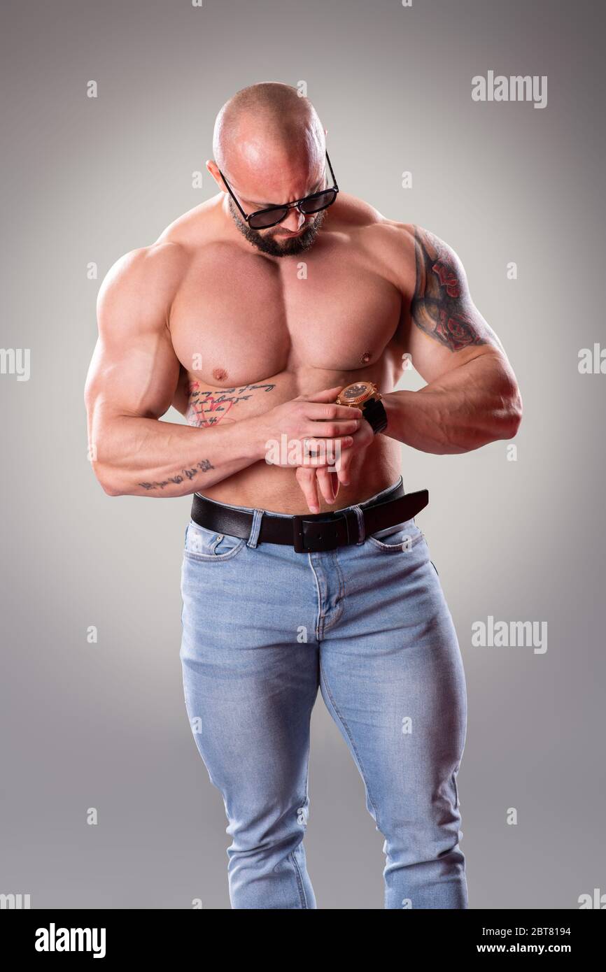 Bodybuider muscoloso sexy guardando il suo orologio su sfondo grigio Foto Stock