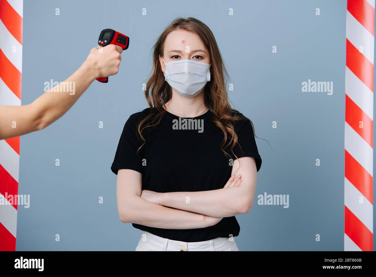 Ragazza si trova al punto di controllo epidemico, il personale misura la sua temperatura Foto Stock