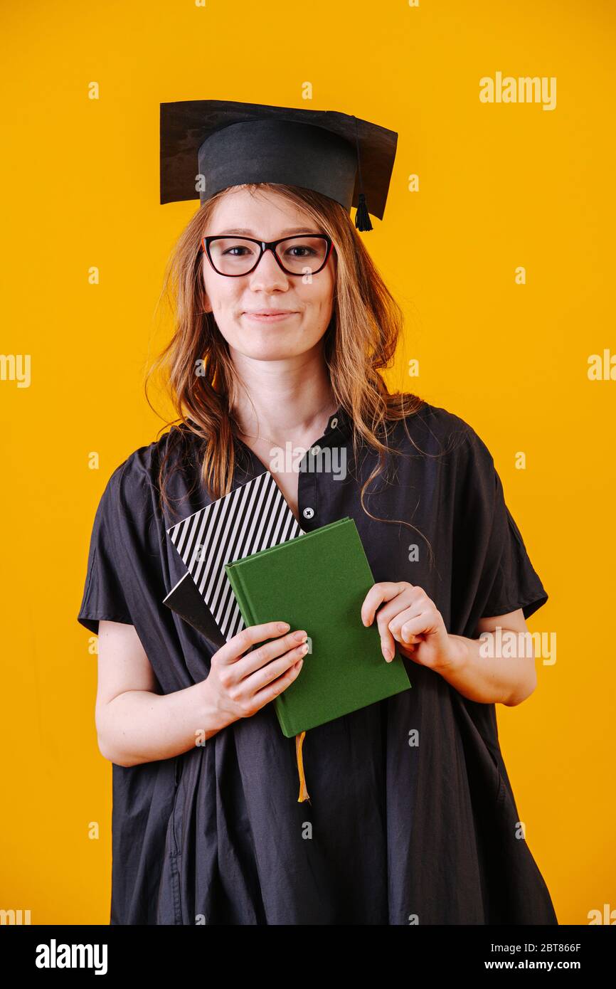 Ragazza in abito accademico con diploma in mano su sfondo giallo Foto Stock