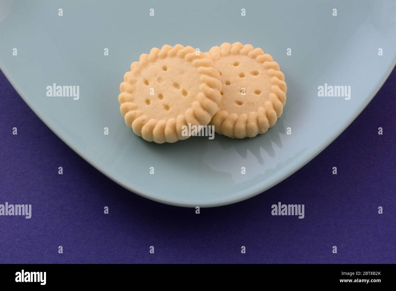 Due biscotti di biscotti di biscotti di shortbread rotondi su piastra blu su sfondo blu scuro Foto Stock
