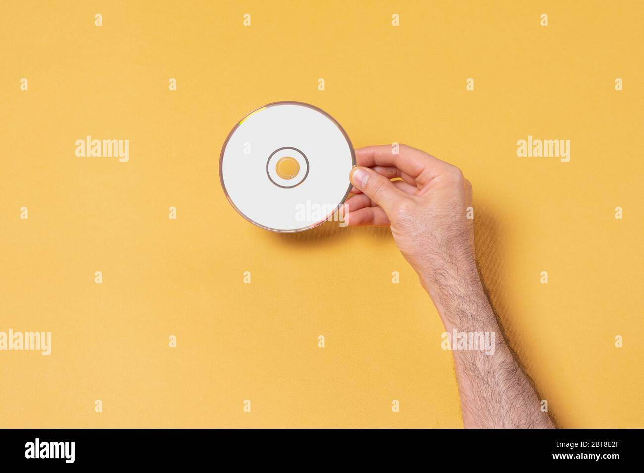 Mano maschio che tiene un CD-DVD davanti a sfondo giallo, modello di serie mock-up pronto per il tuo design, percorso di selezione copertina incluso Foto Stock