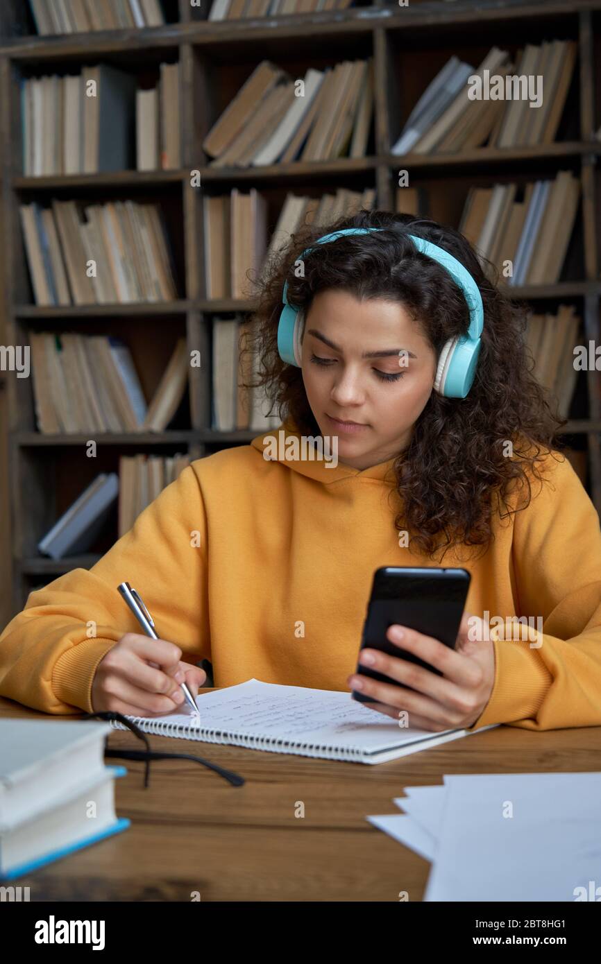 Hispanic teen girl indossare cuffie tenere telefono distanza imparare in app mobile. Foto Stock