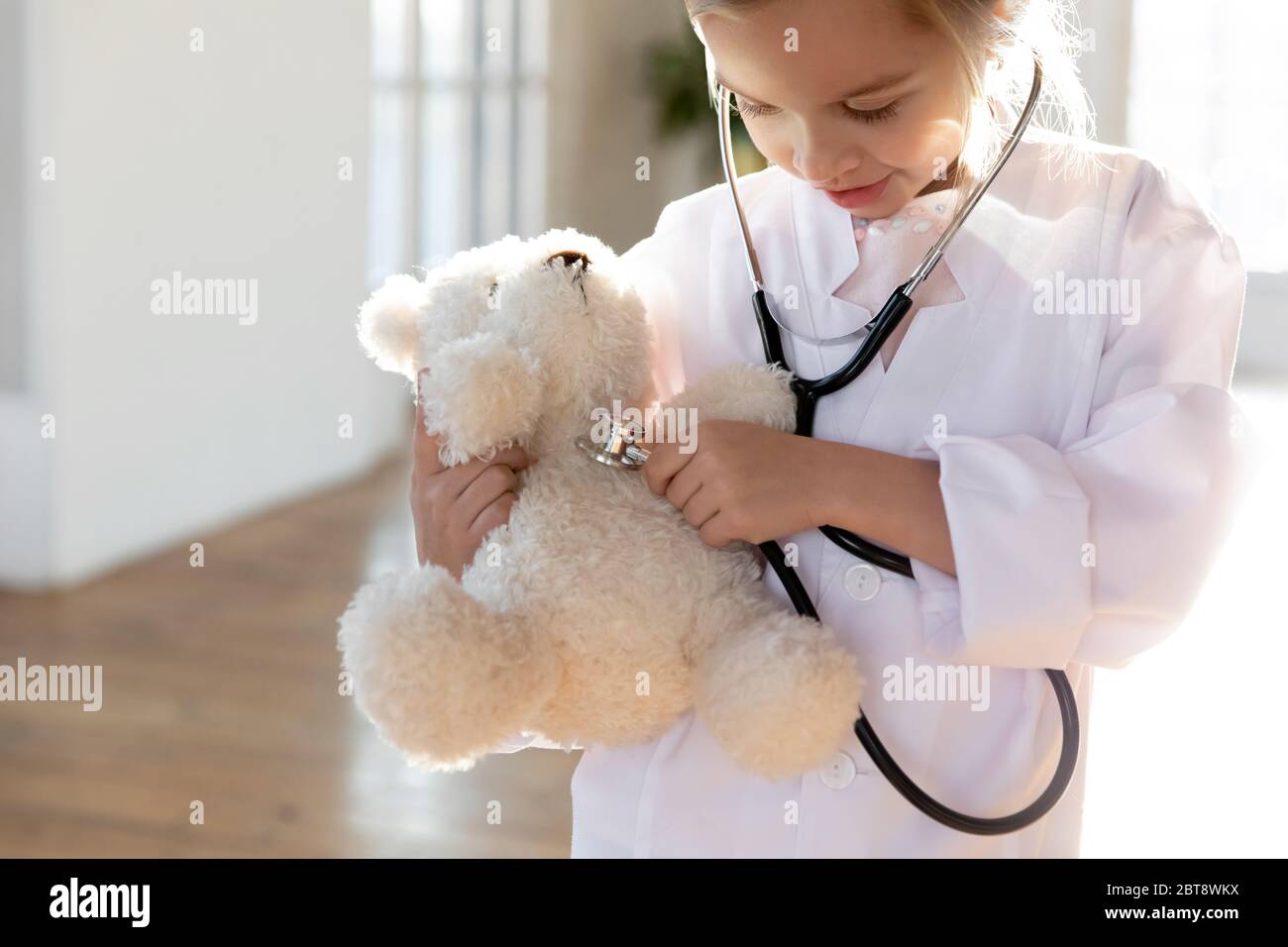 Bambina in uniforme bianca esamina peluche giocattolo Foto Stock