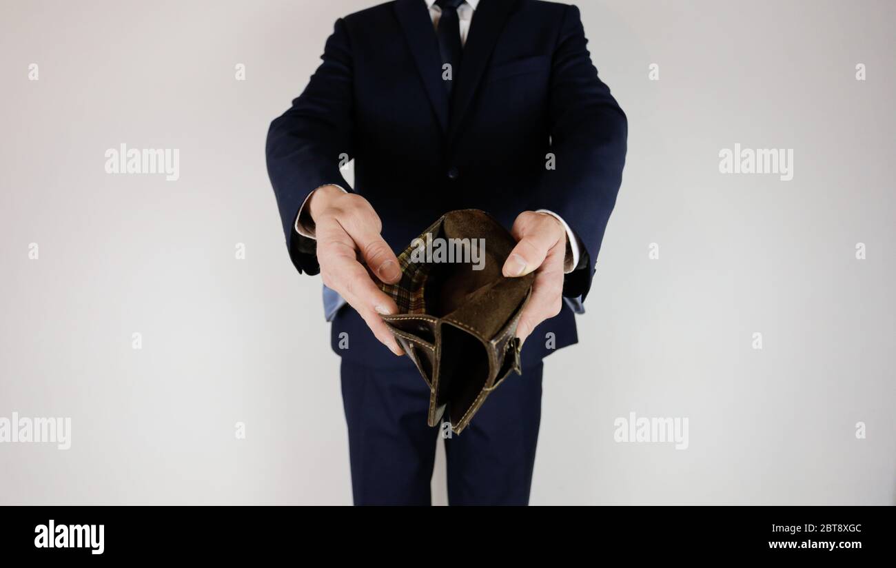 Un uomo in un vestito da lavoro tiene in mano un portafoglio vuoto senza soldi. Crisi finanziaria. Fallimento nel commercio. Il datore di lavoro è deluso. Foto Stock