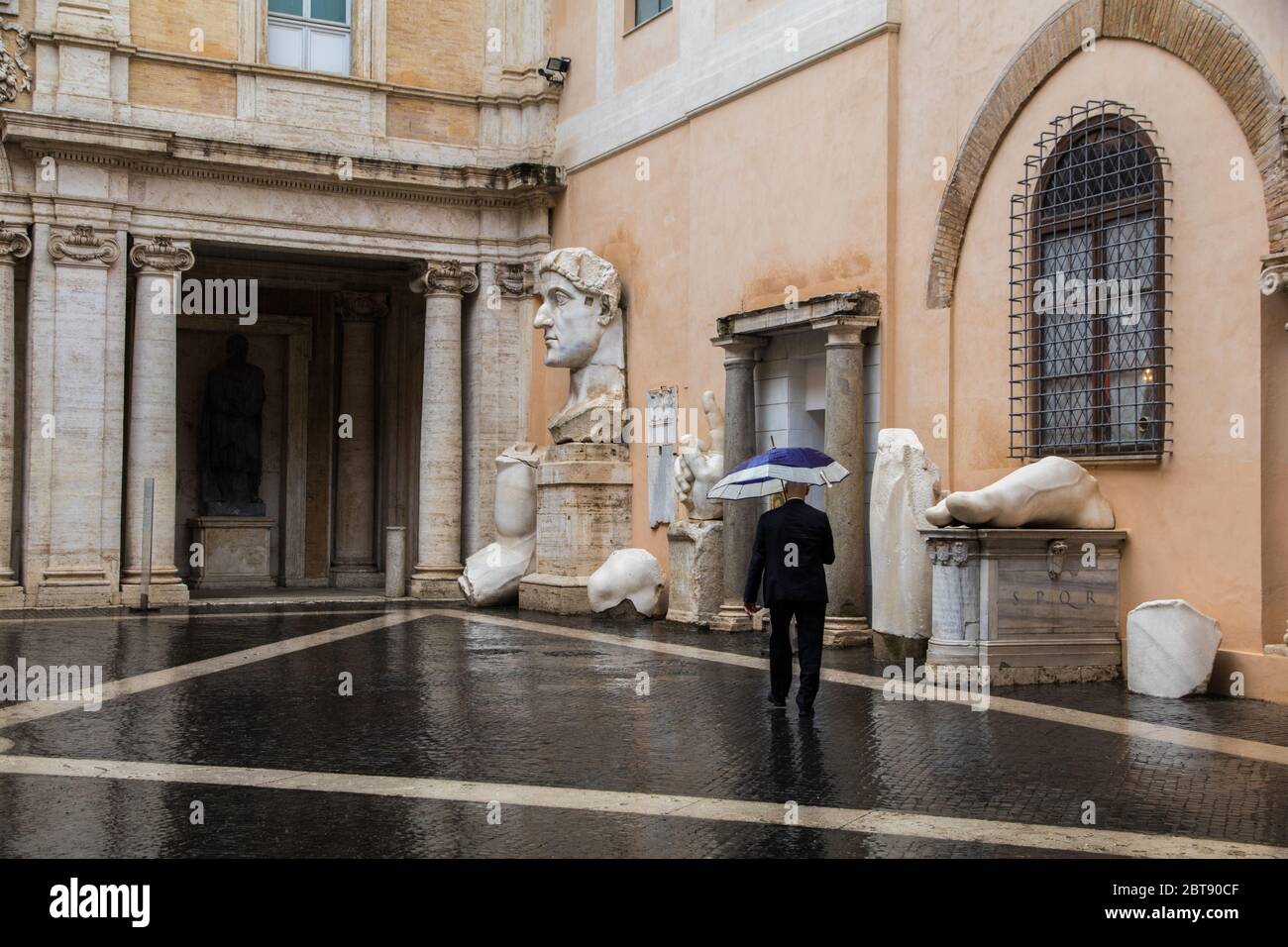 Uomo con ombrello nel cortile del Museo Capitolino di Roma Foto Stock