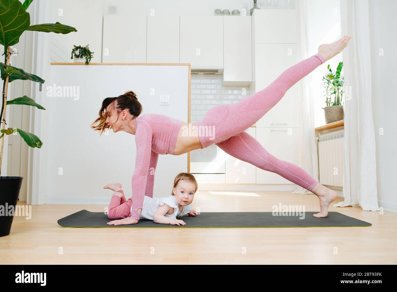 Una giovane madre in abbigliamento sportivo pratica ginnastica a casa Foto Stock