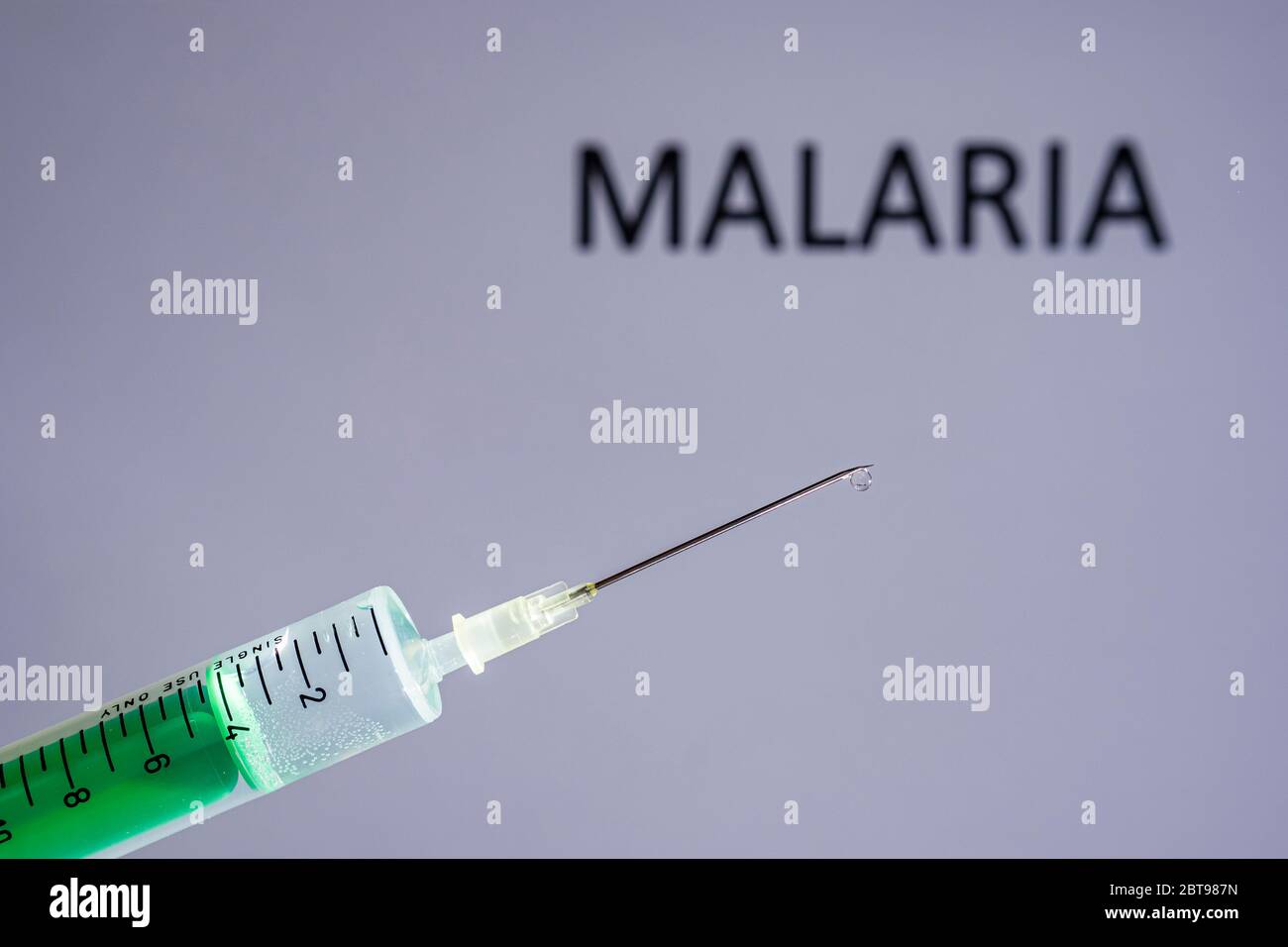 Questa illustrazione mostra una siringa monouso con ago ipodermico, MALARIA scritta su una tavola grigia dietro Foto Stock