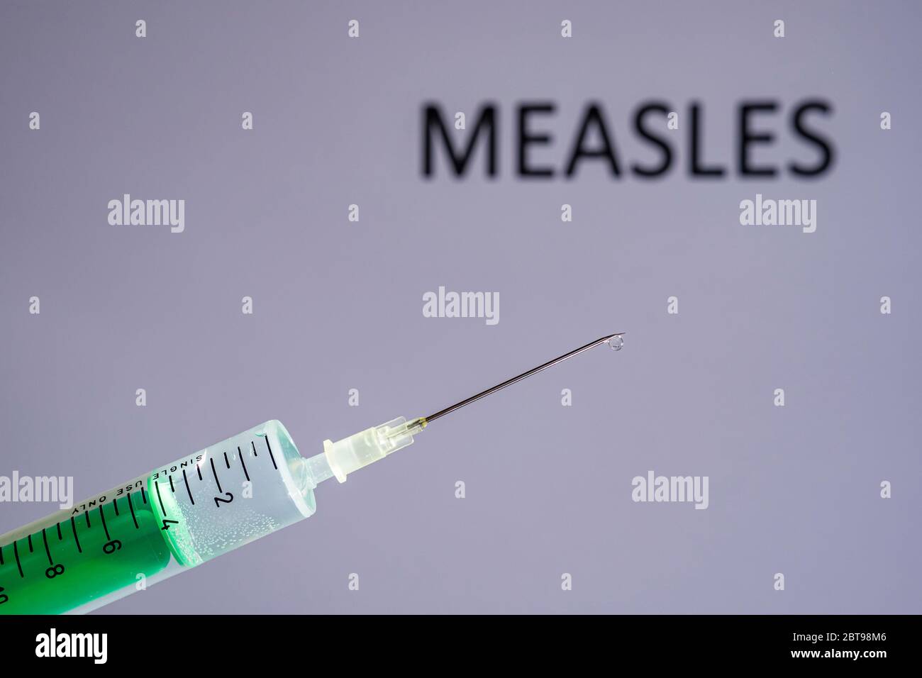 Questa figura mostra una siringa monouso con ago ipodermico, MORBILLO scritto su una tavola grigia dietro Foto Stock