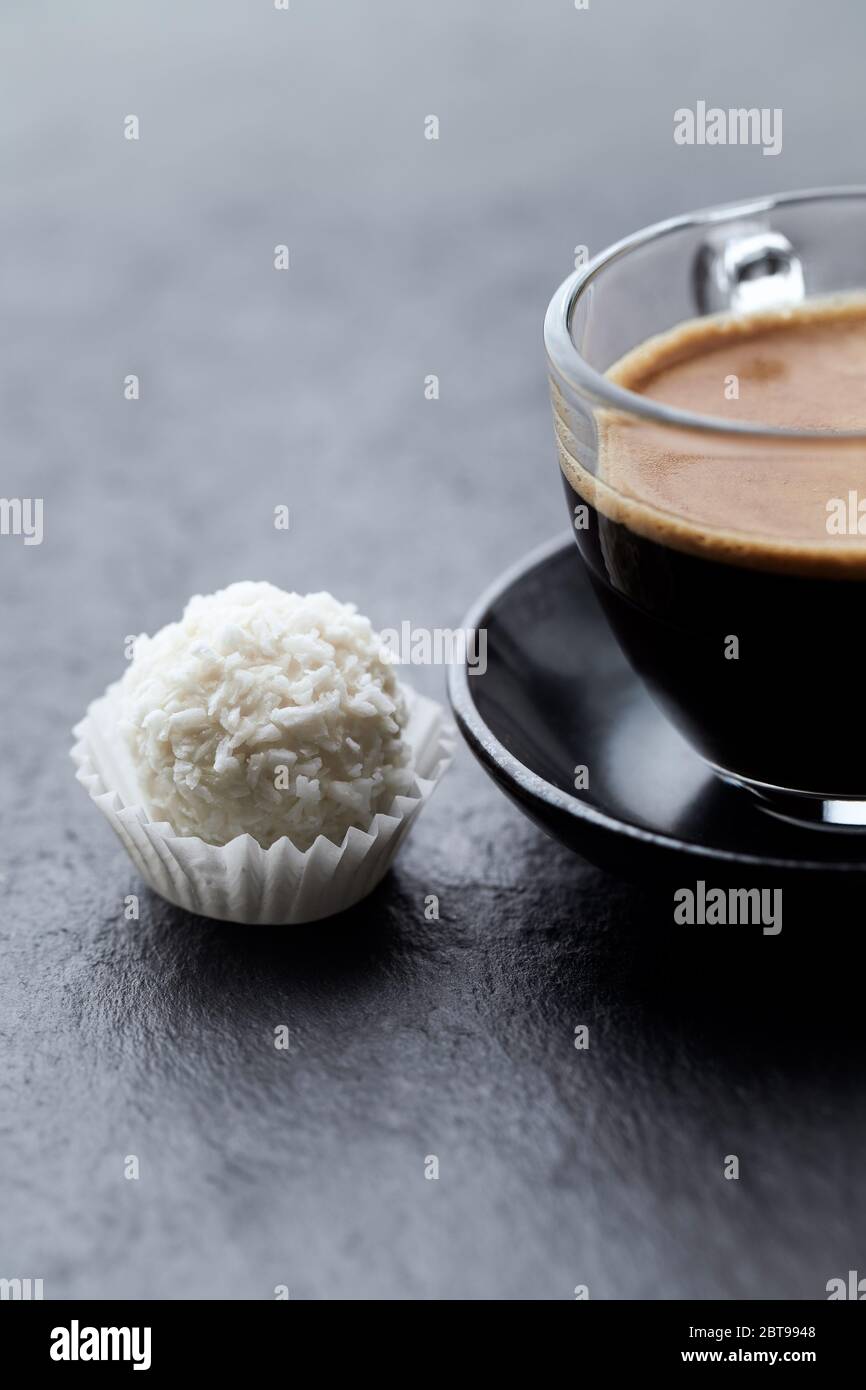 Pralina e caffè in una tazza di vetro su fondo di pietra. Primo piano. Foto Stock
