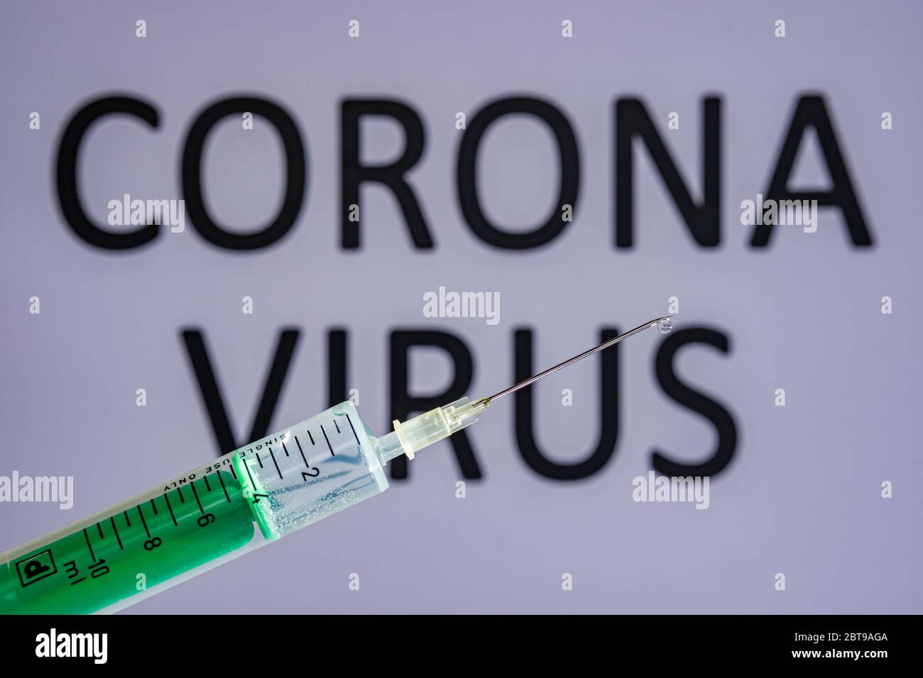 Questa illustrazione mostra una siringa monouso con ago ipodermico, IL VIRUS CORONA scritto su una tavola grigia dietro Foto Stock
