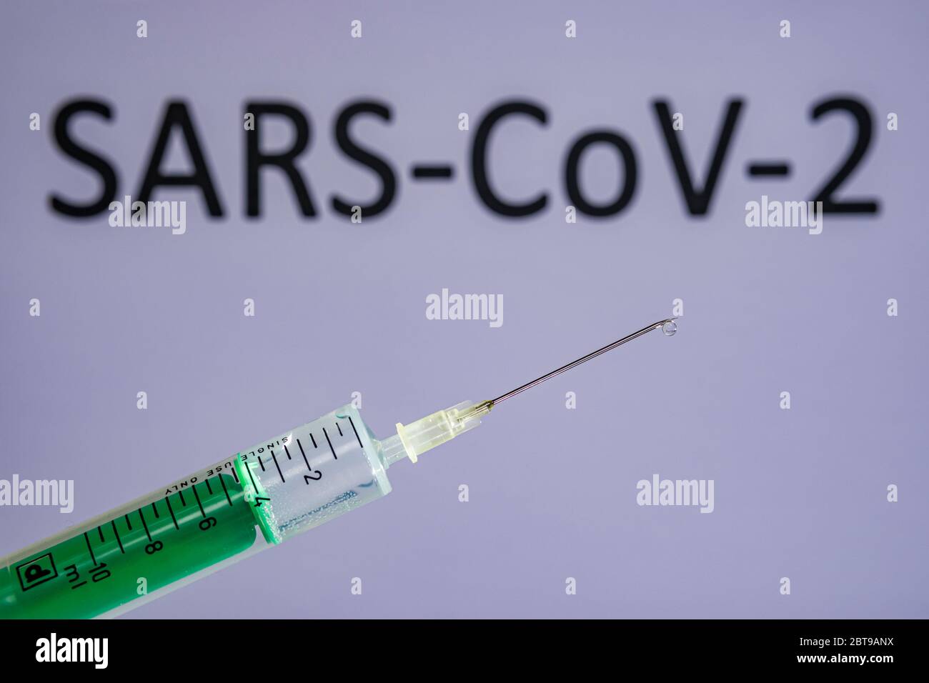 Questa figura mostra una siringa monouso con ago ipodermico, SARS-COV-19, scritta su una tavola grigia dietro Foto Stock
