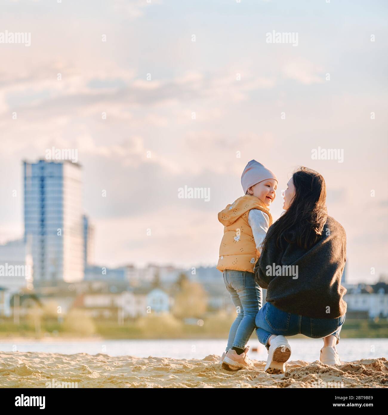 mamma e figlia si trovano con le spalle alla spiaggia sullo sfondo del paesaggio cittadino Foto Stock