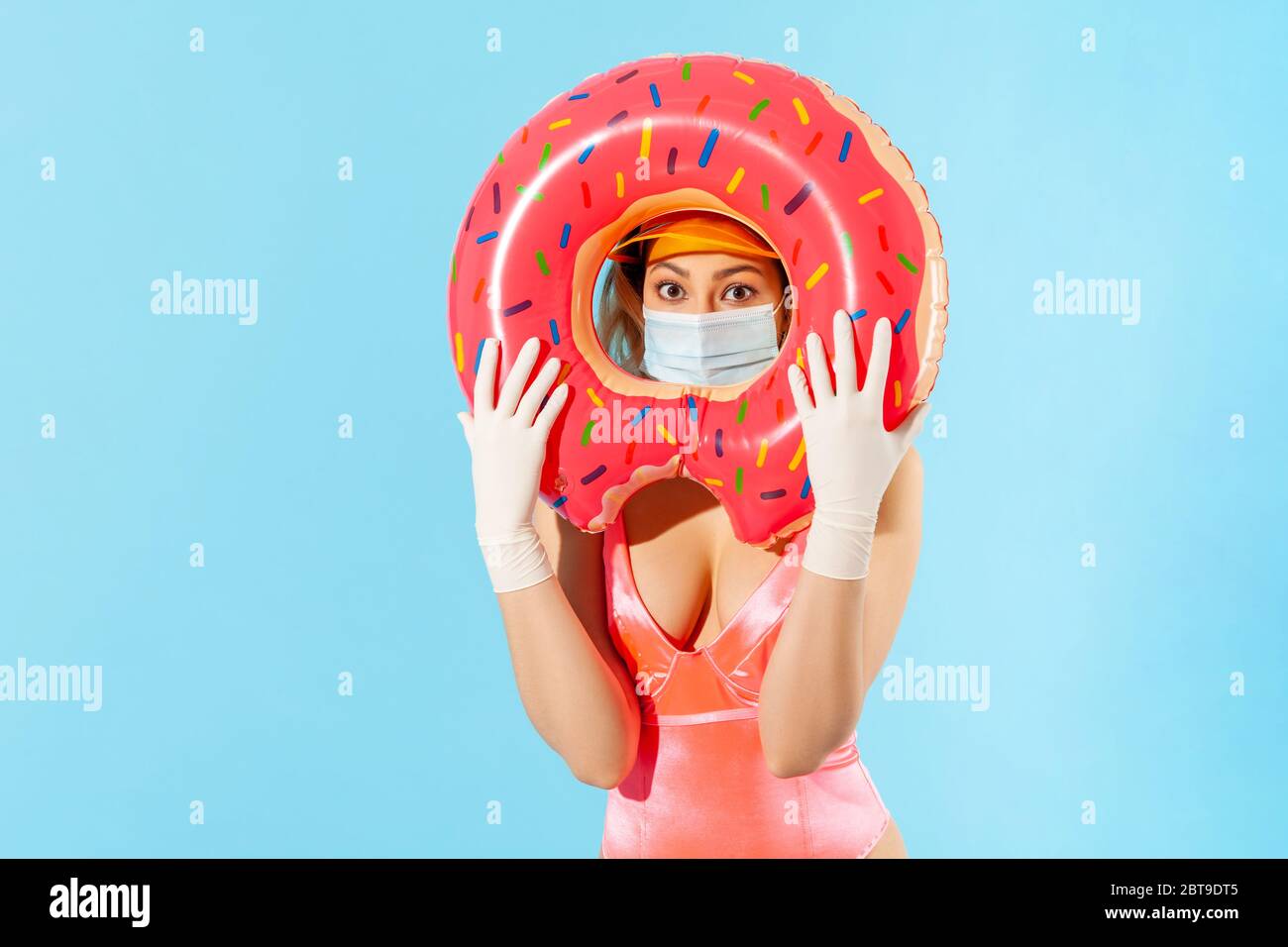 Donna in costume da bagno guardando attraverso l'anello di gomma, indossando maschera igienica e guanti chirurgici per prevenire il coronavirus contagioso sulla spiaggia del resort, riposo Foto Stock
