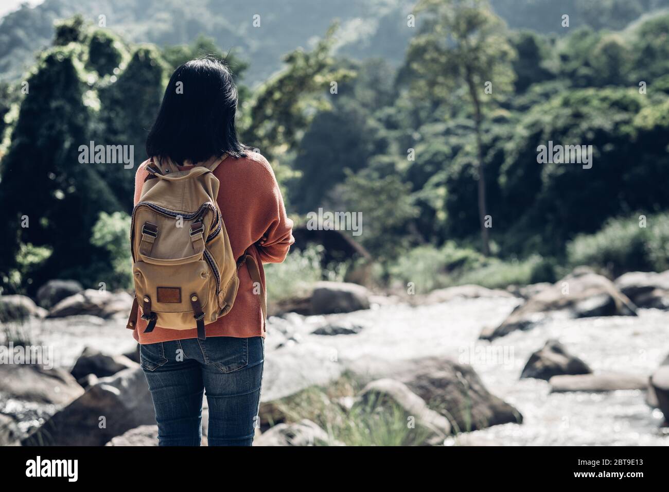 Viaggiatore asiatico donna in piedi su roccia a vista del paesaggio di verde foresta pluviale e acqua corrente in giornata di sole a Forest.backpacker esplorare la vita della natura Foto Stock