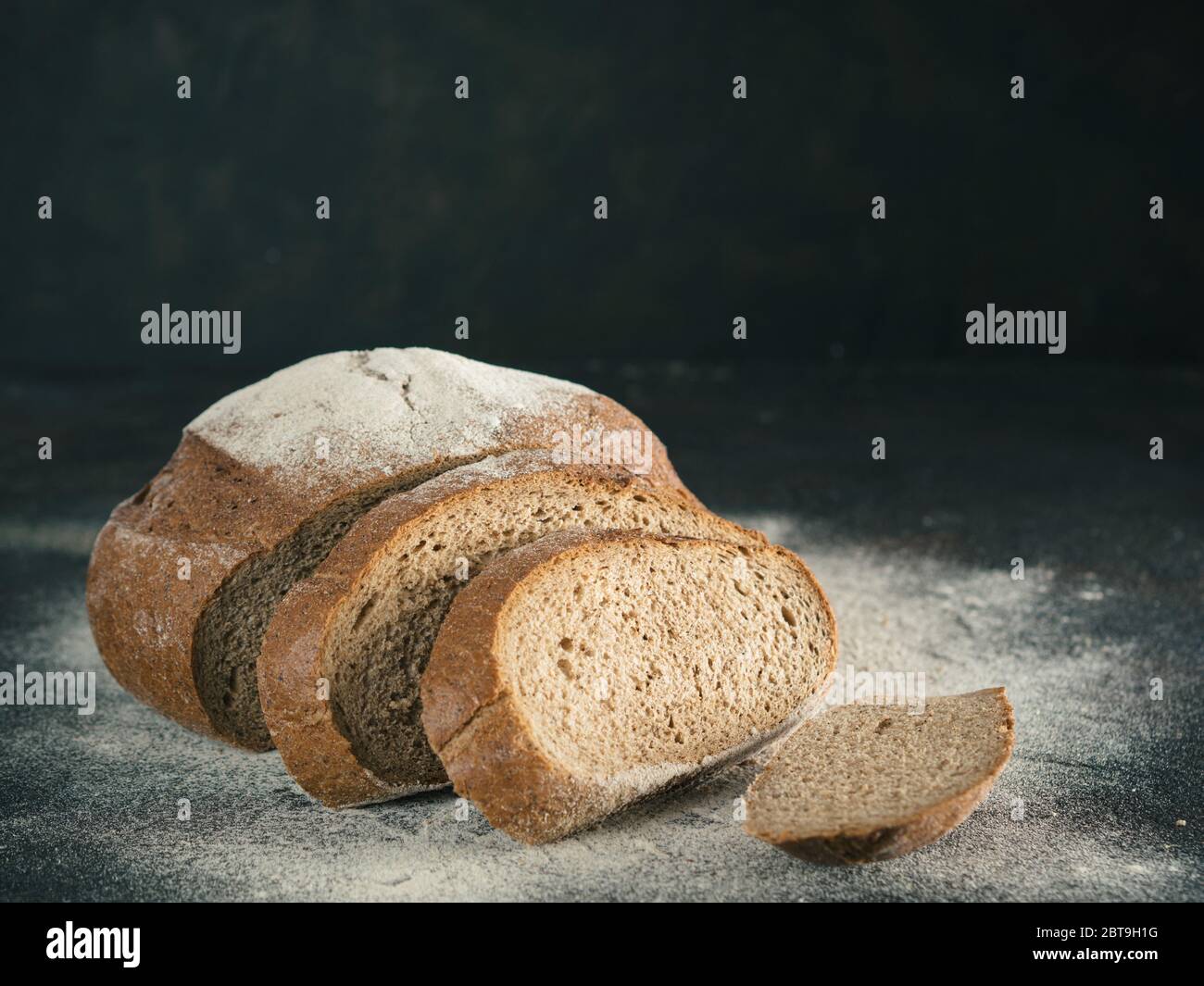 Fette di pasta madre casalinga pane di segale con la farina di segale sul nero testurizzato sfondo. Copia dello spazio. Tasto basso Foto Stock