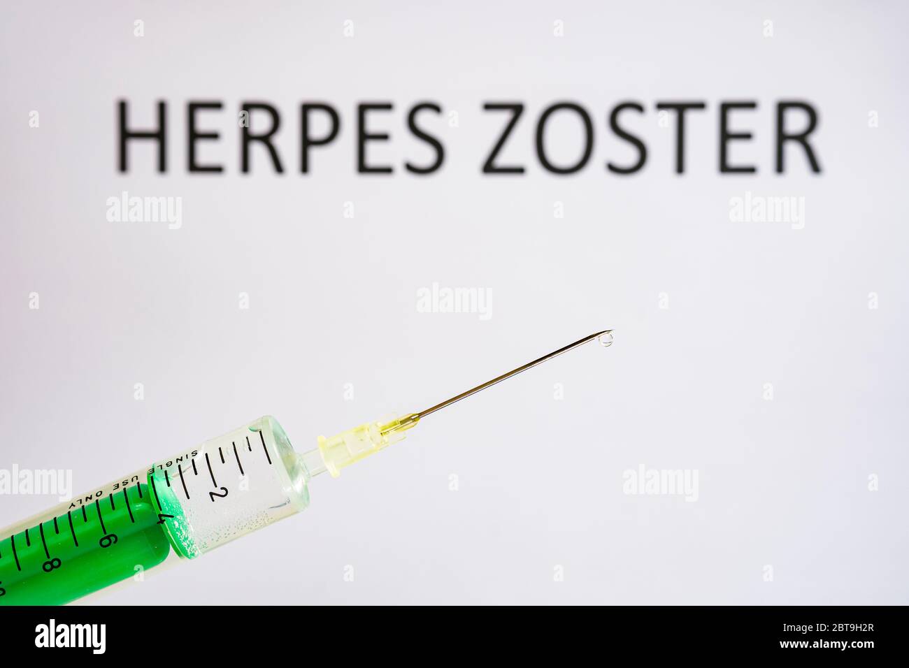 Questa illustrazione della foto mostra una siringa monouso con ago ipodermico, HERPES ZOSTER scritto su una lavagna bianca dietro Foto Stock