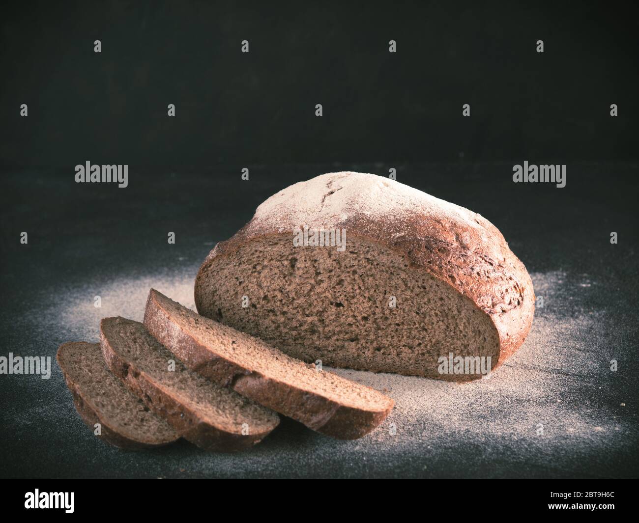 Fette di pasta madre casalinga pane di segale con la farina di segale sul nero testurizzato sfondo. Copia dello spazio. Tasto basso immagine dai toni Foto Stock